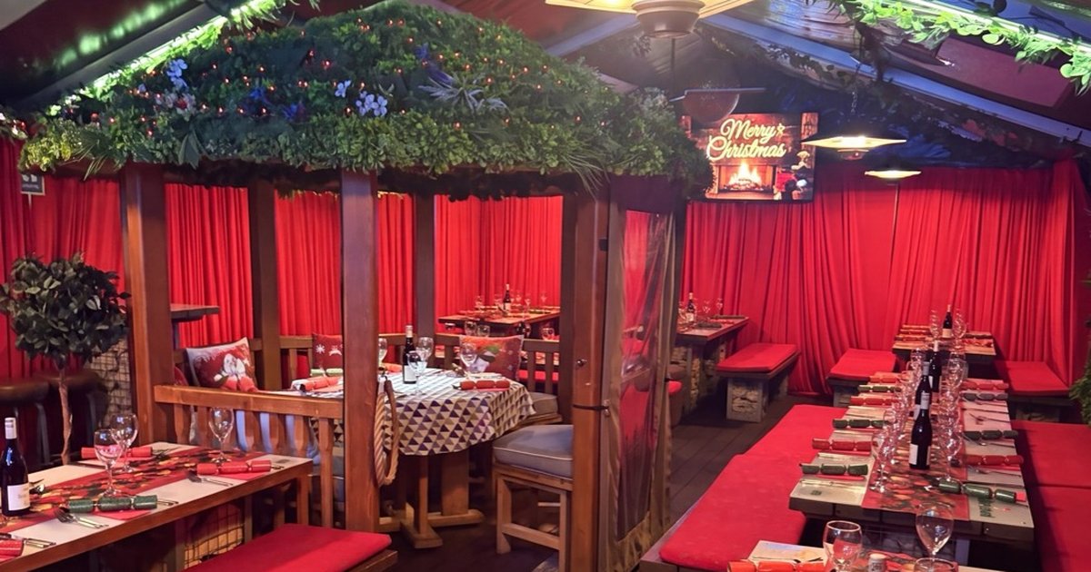 The heated garden marquee at Fizzy Moon, Leamington Spa, dressed for Christmas parties with red curtains, garlands and tables set with crackers.